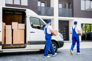 Two removal company workers unloading boxes from minibus into new home.